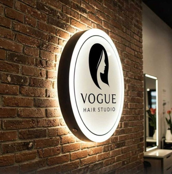 Custom round acrylic salon sign with elegant halo LED backlighting mounted on a brick wall for professional business branding.