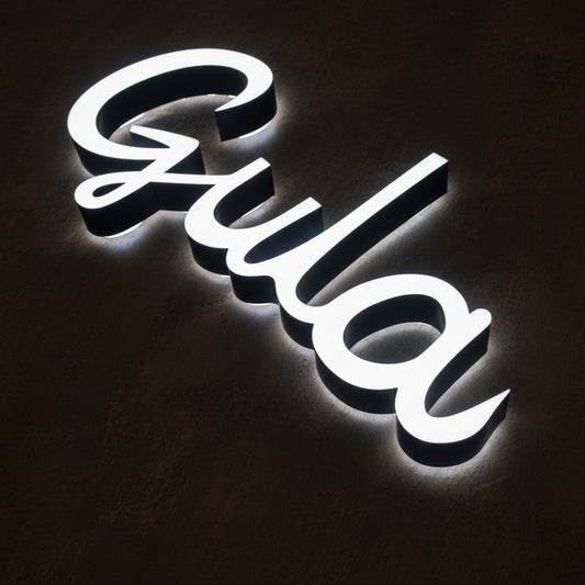 Custom LED halo-lit script letter sign with elegant cursive typography and soft white backlighting.