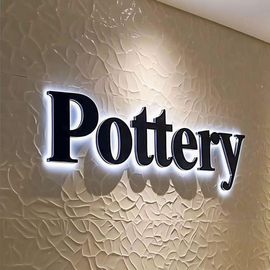 Custom Pottery acrylic letter sign with white halo LED backlighting mounted on a textured decorative wall.