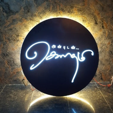 Custom round LED acrylic sign board with illuminated logo design and warm halo backlighting mounted on a textured wall.