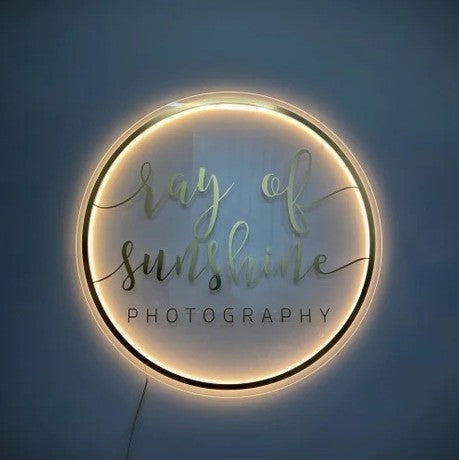 Custom round acrylic photography sign with warm halo LED backlighting, mounted as an elegant studio branding display.