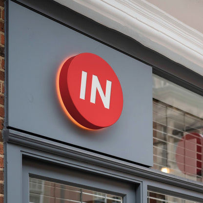 Modern circular business branding sign featuring illuminated white lettering and halo glow