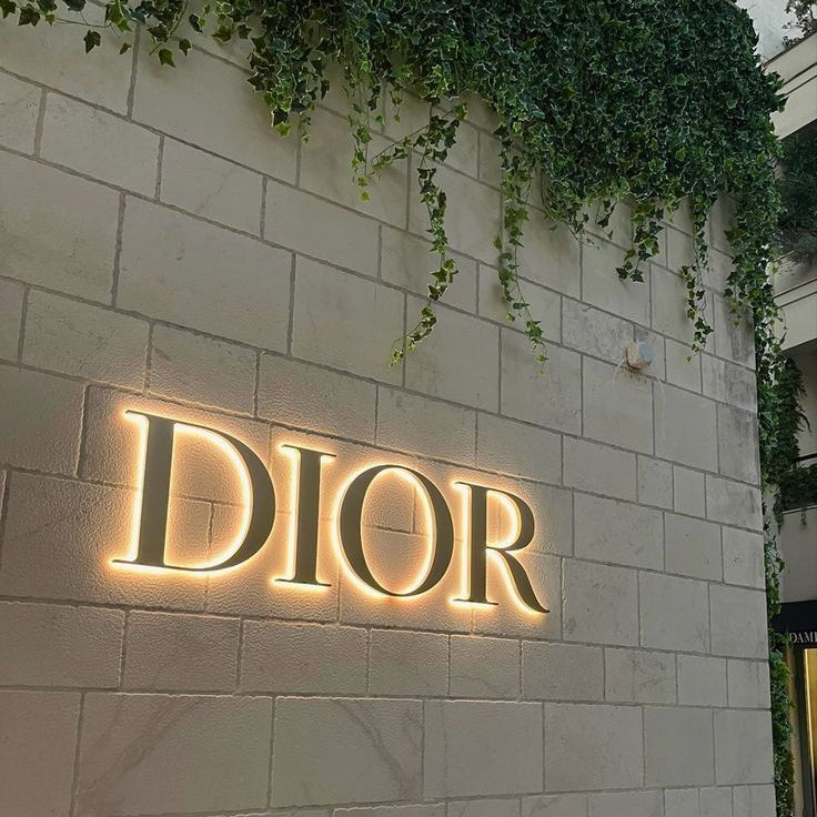 Elegant DIOR-inspired LED acrylic wall sign with warm white backlit glow mounted on a stone wall for luxury interior décor.